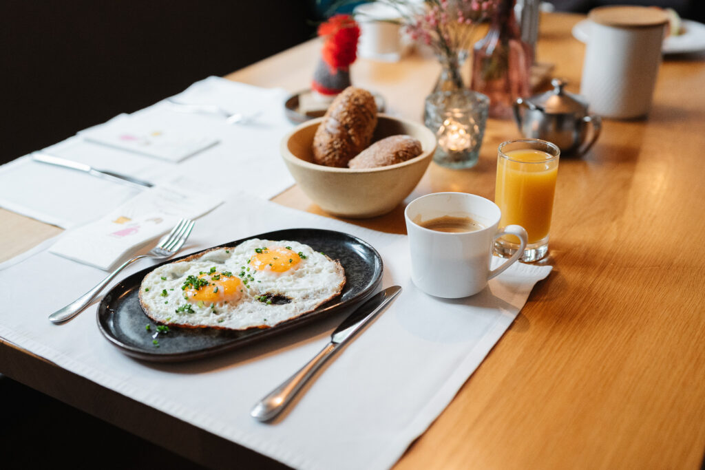 Teller mit zwei Spiegeleiern, Brot, Saft und Kaffee an einem Tisch in einem Restaurant in St. Anton.