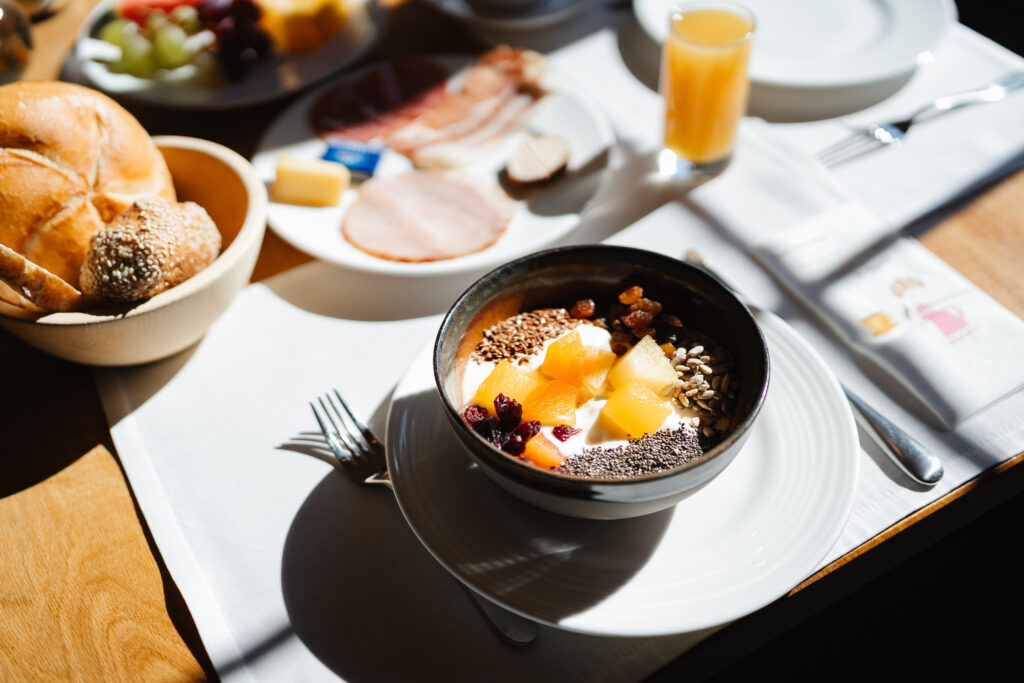 Eine Schale Müsli mit Obst, Brötchen und Saft an einem gemütlichen Frühstückstisch in einem Restaurant in St. Anton.