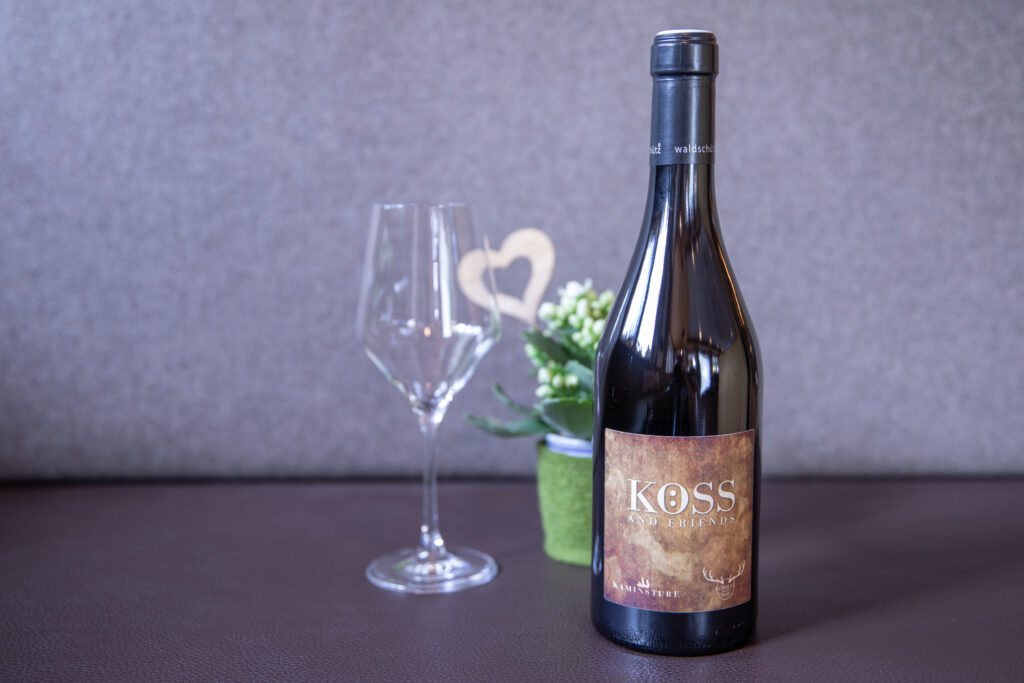 Eine Weinflasche mit der Aufschrift Koss and Friends in der Bar St. Anton am Arlberg, daneben ein Glas und eine Pflanze.